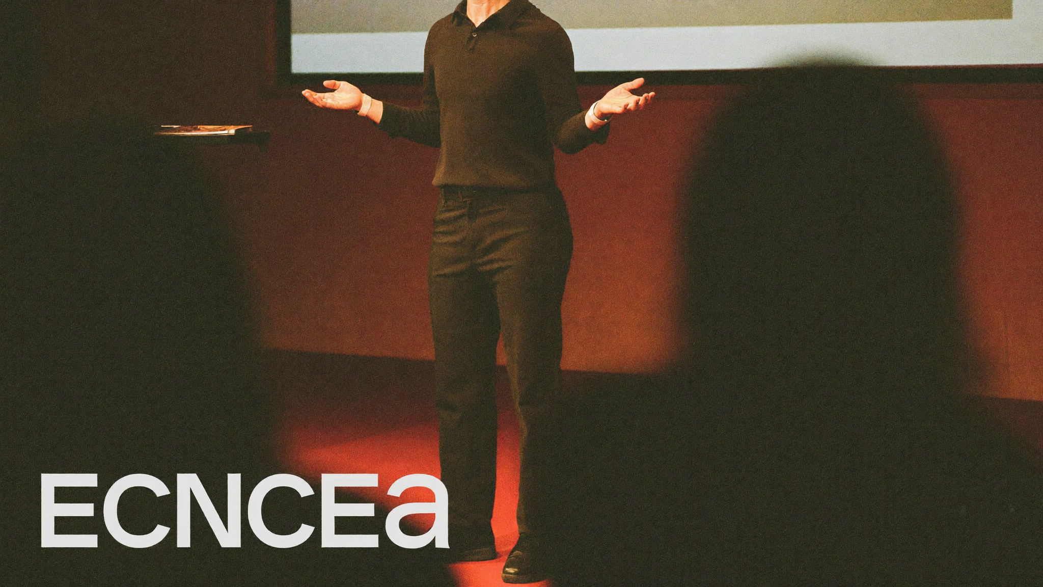 Speaker gesturing on stage under warm spotlight