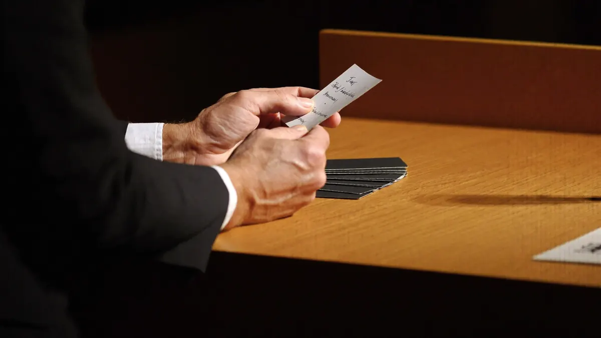 Close-up of a speaker’s hands holding note cards over a wooden lectern